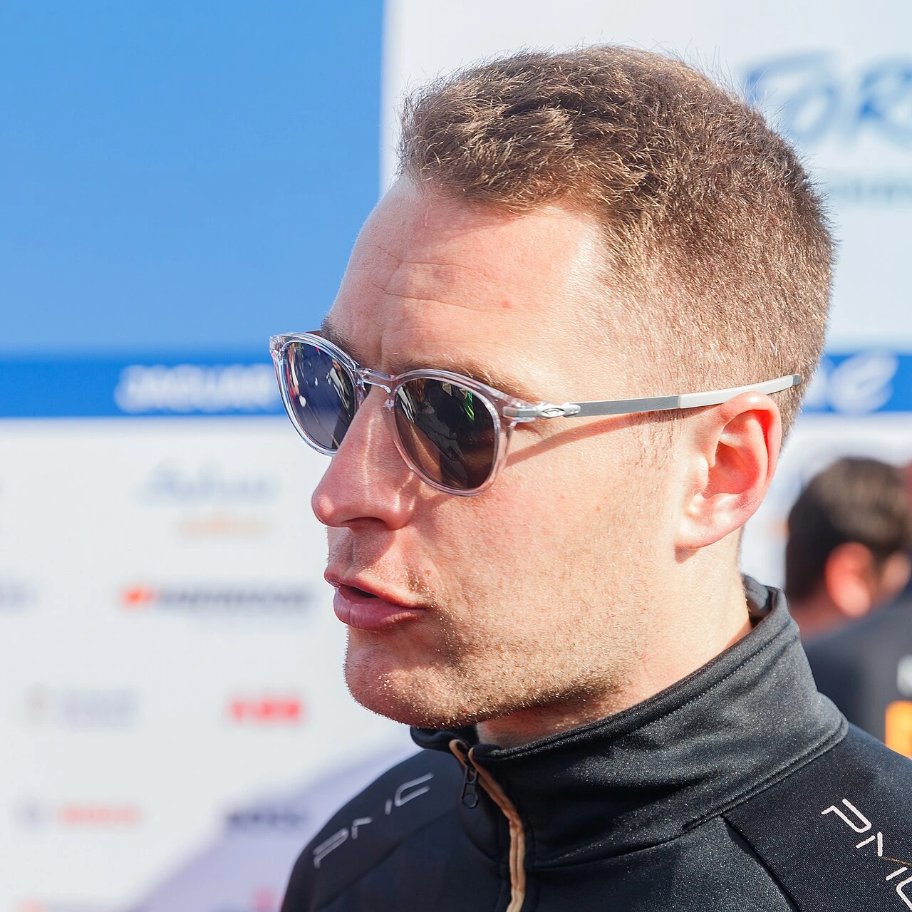 Stoffel Vandoorne at a Formula E event wearing sunglasses and a black racing suit.