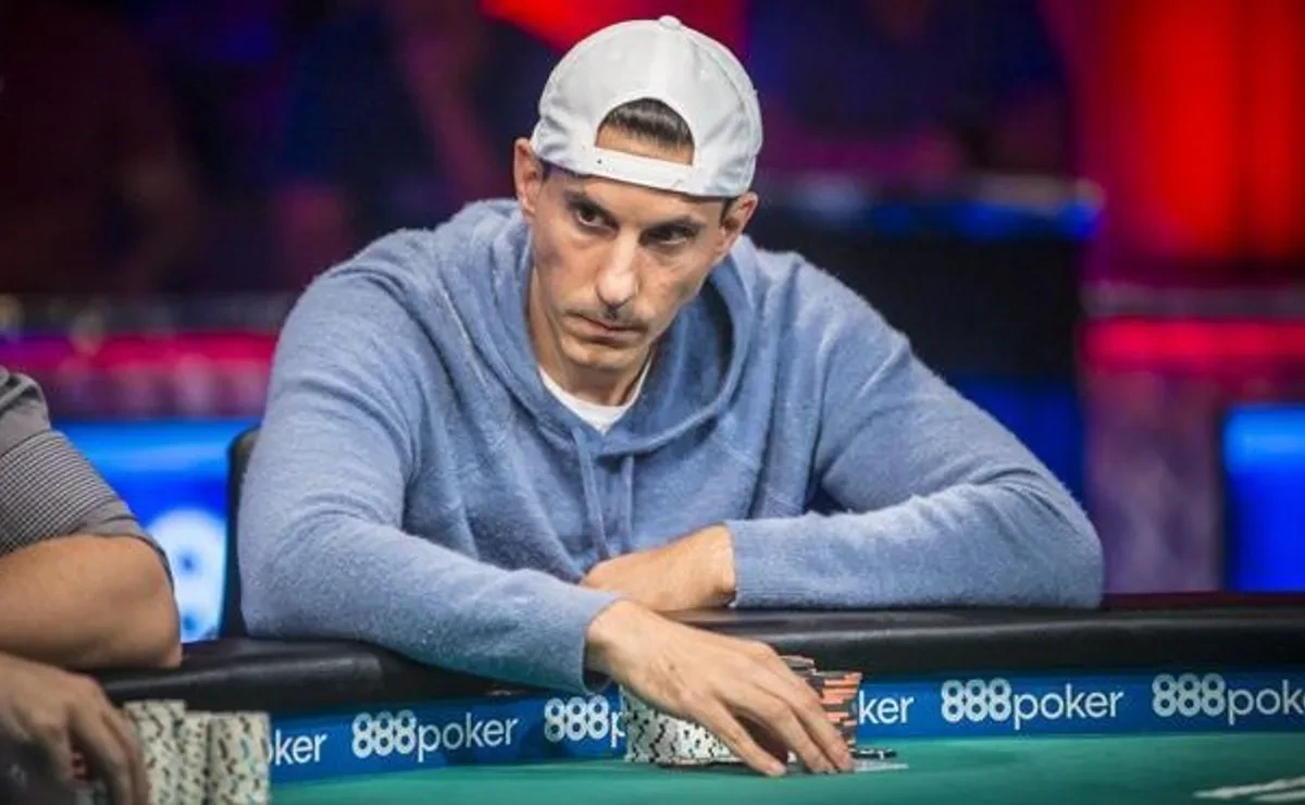 Haralabos Voulgaris seated at a poker table in a blue hoodie and backward white cap, focused on the game.