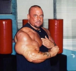 Gregg Valentino posing in a gym, showing his heavily muscled arms.