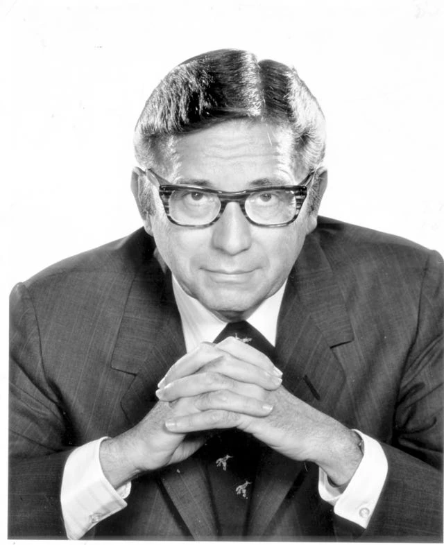 Black-and-white portrait of Beurt Richard SerVaas in a suit and glasses, hands clasped.