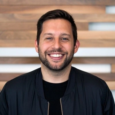 Headshot of Chris Vaccarino smiling against a wood slat background.