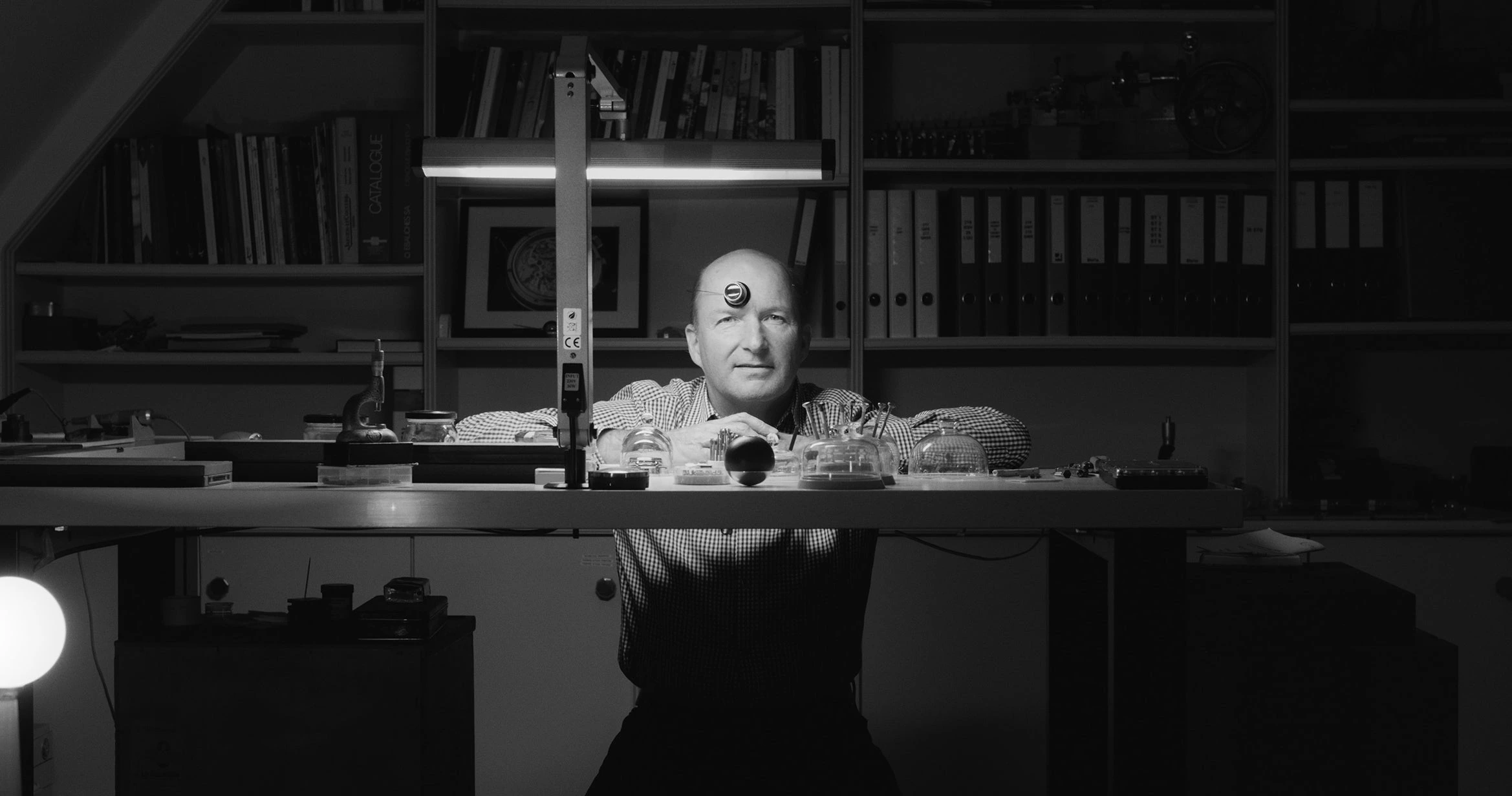 Black-and-white portrait of Kari Voutilainen seated at a watchmaking bench in his workshop