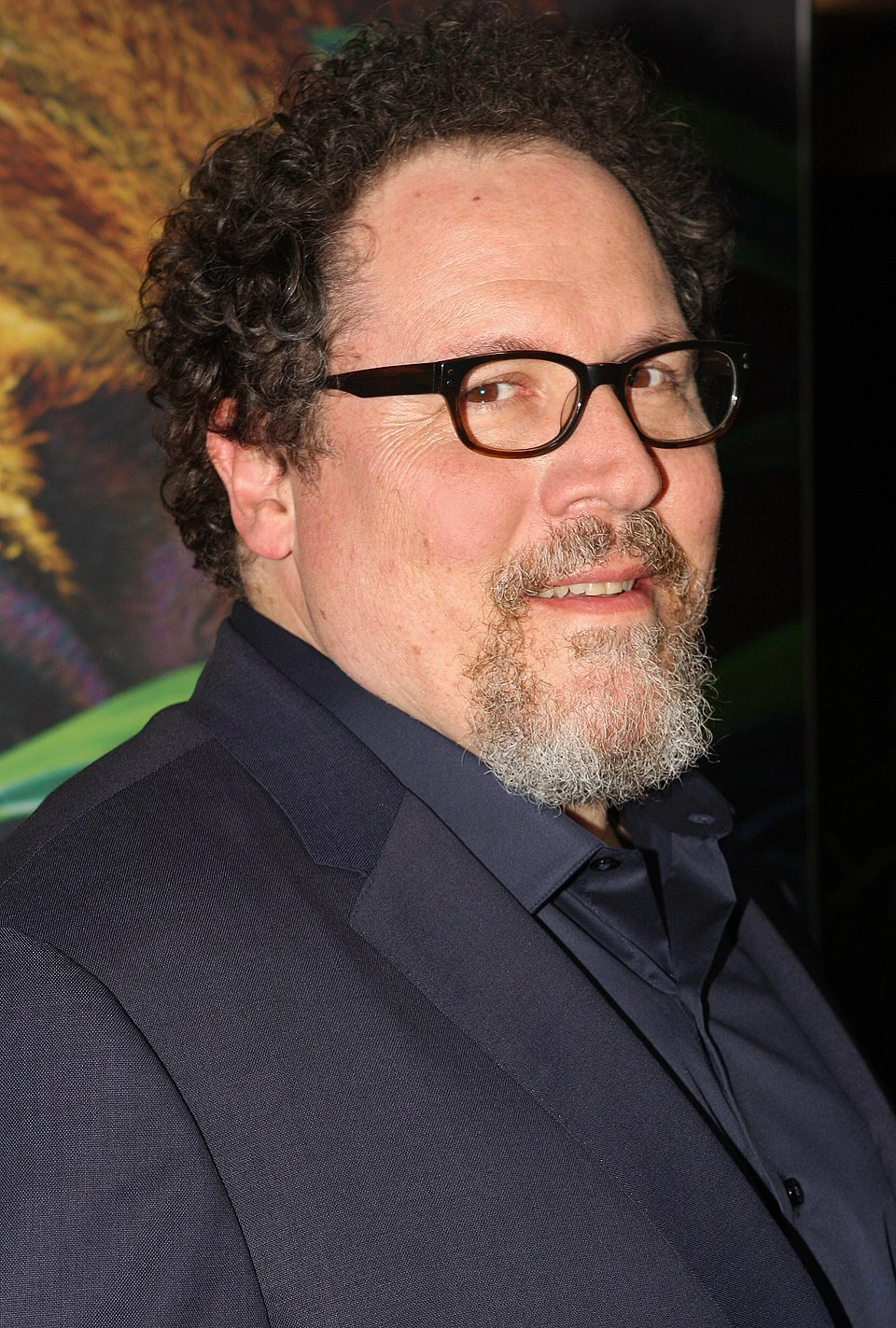 Portrait photo of filmmaker Jon Favreau in a dark suit and glasses at an event